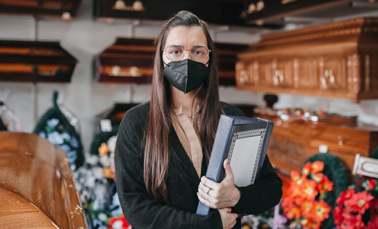 Funeral Director wearing mask in funeral home surrounded by flower and casket options