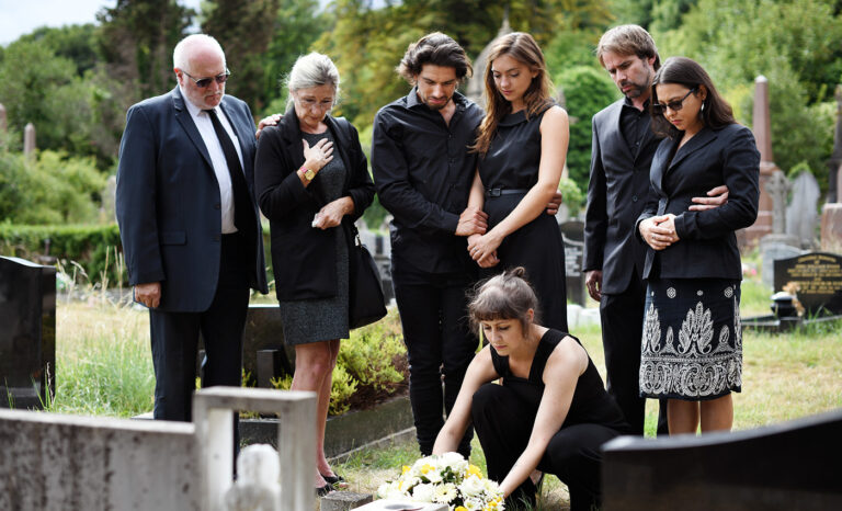 Woman placing flowers on grave with family surrounding her