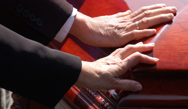Two hands on a wooden casket