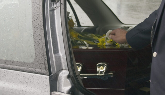 Man placing his hand on a casket in back of vehicle